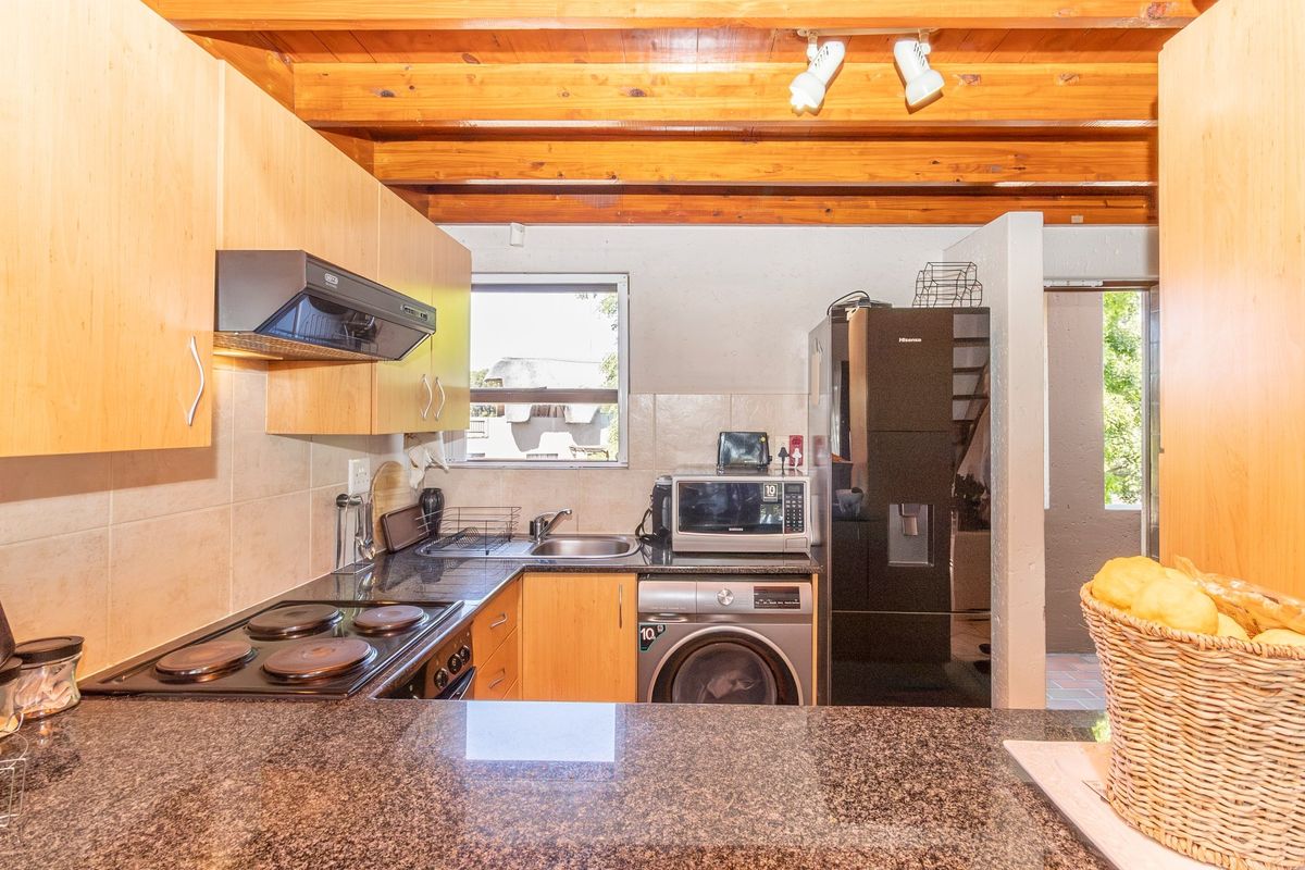 Functional kitchen featuring granite countertops, built-in cabinetry, electric hob, extractor fan, and exposed timber ceiling beams.