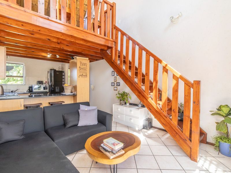 Open plan living area featuring a wooden staircase leading to a mezzanine level, adjacent to a functional kitchen with tiled flooring.