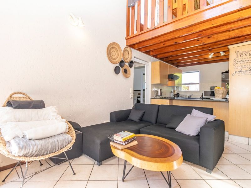 Open plan living area featuring a wooden mezzanine loft level, tiled flooring, and a functional kitchen with built-in cabinetry and counter space.