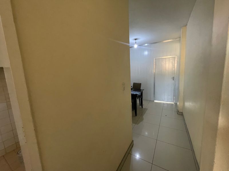 A narrow hallway with tiled flooring leading towards an internal door, showing signs of wear on the wall surfaces.