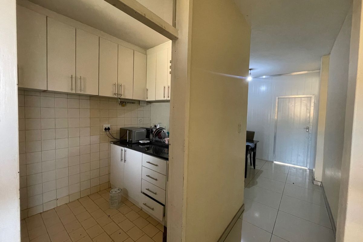 A compact kitchen featuring built-in cabinetry, stone countertops, and tiled finishes, leading into an adjacent living area with tiled flooring.