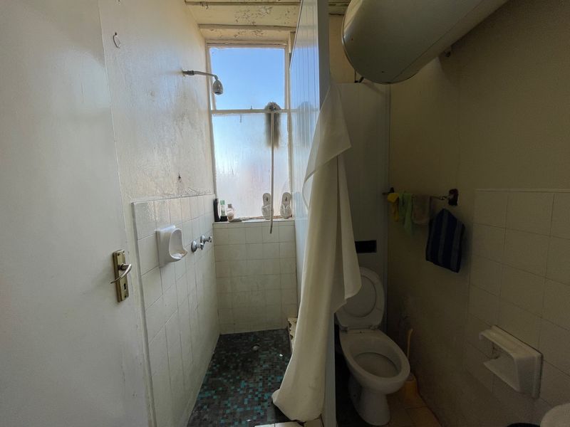 A compact bathroom featuring a shower area, toilet, and wall-mounted water heater, requiring significant cosmetic updates and maintenance to improve its condition.