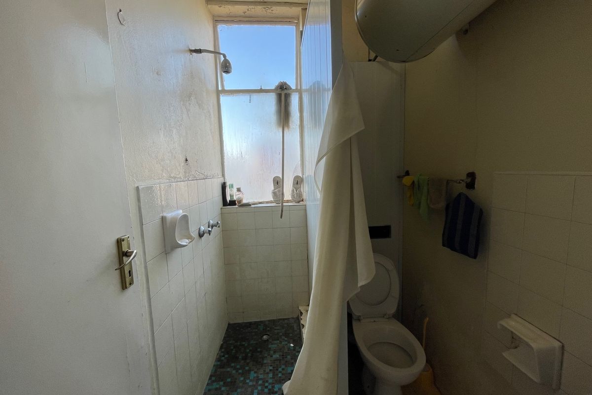 A compact bathroom featuring a shower area, toilet, and wall-mounted water heater, requiring significant cosmetic updates and maintenance to improve its condition.