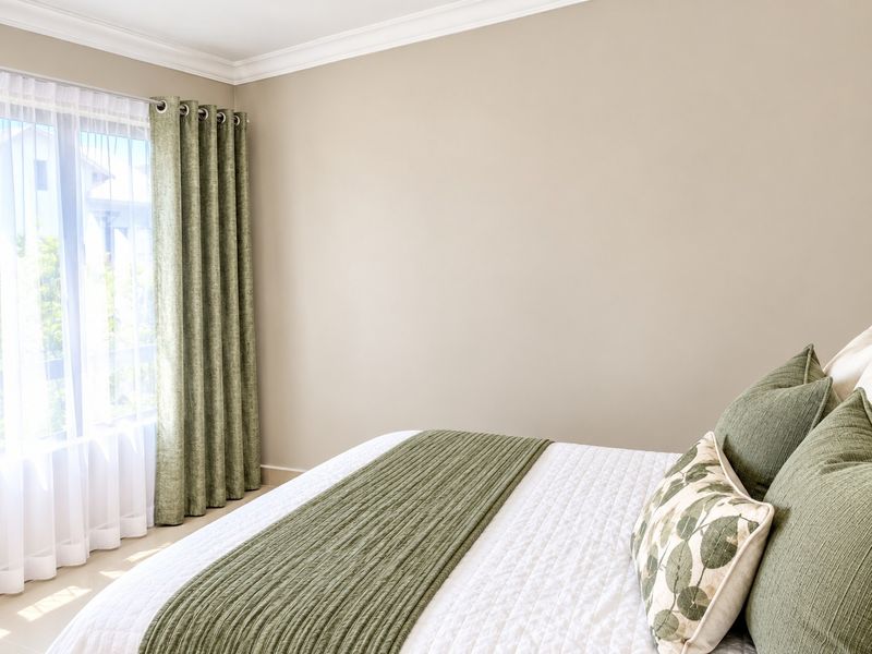 A bright and well-maintained bedroom featuring neutral wall tones, crown molding, and tiled flooring with natural light from the window.