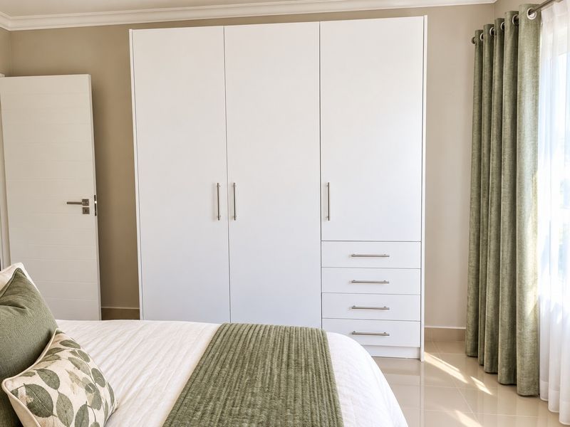 A well-maintained bedroom featuring a large, modern white built-in wardrobe with integrated drawers and neutral tiled flooring.