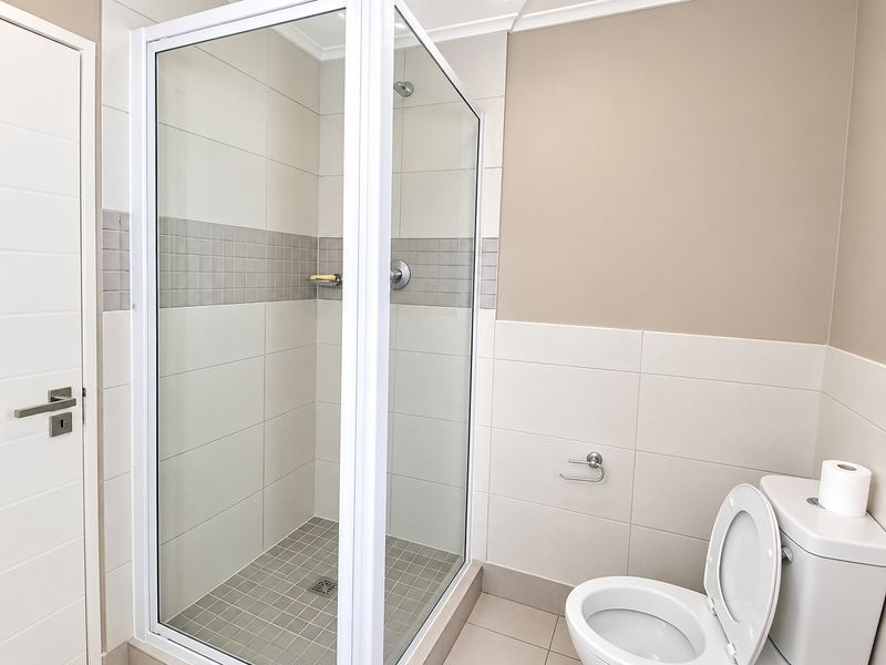 A clean and modern bathroom featuring a glass-enclosed shower, neutral wall tiling, and a standard toilet suite.