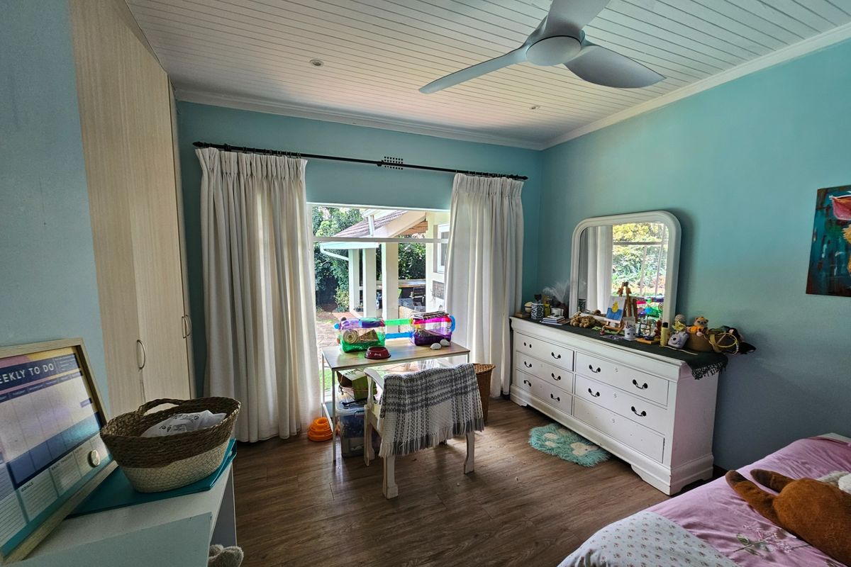 A well-lit bedroom featuring laminate flooring, built-in cupboards, and a ceiling fan, with direct access to an outdoor patio area.