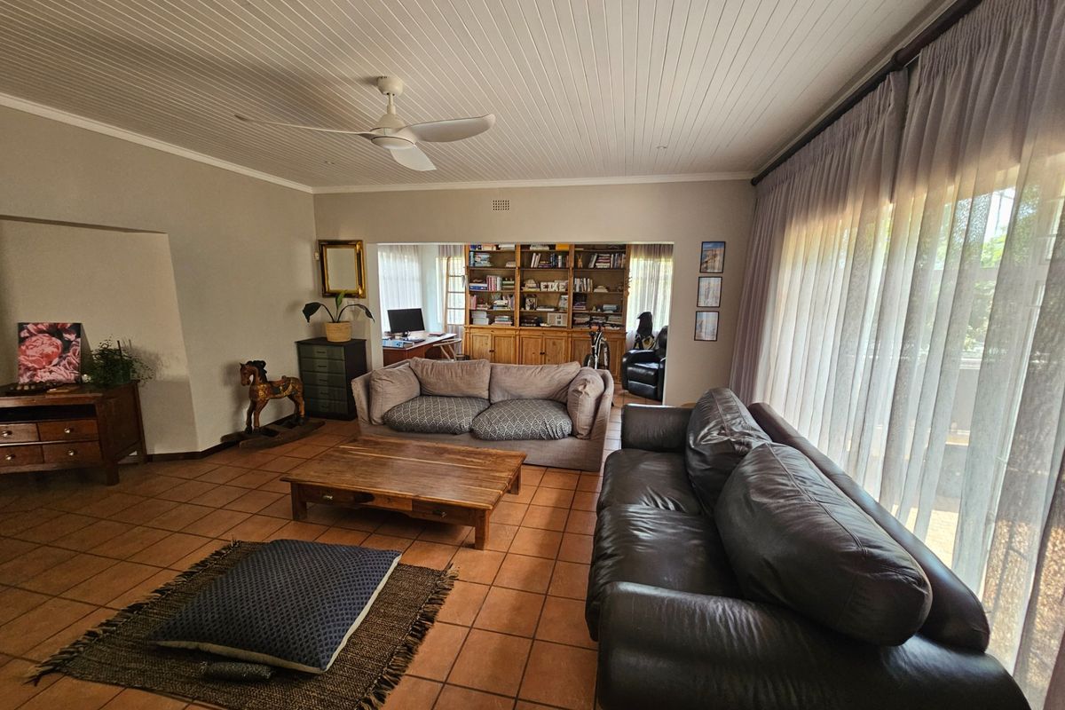 Spacious living room featuring terracotta floor tiles, a tongue and groove ceiling with a fan, and a built-in shelving unit in the adjacent study area.