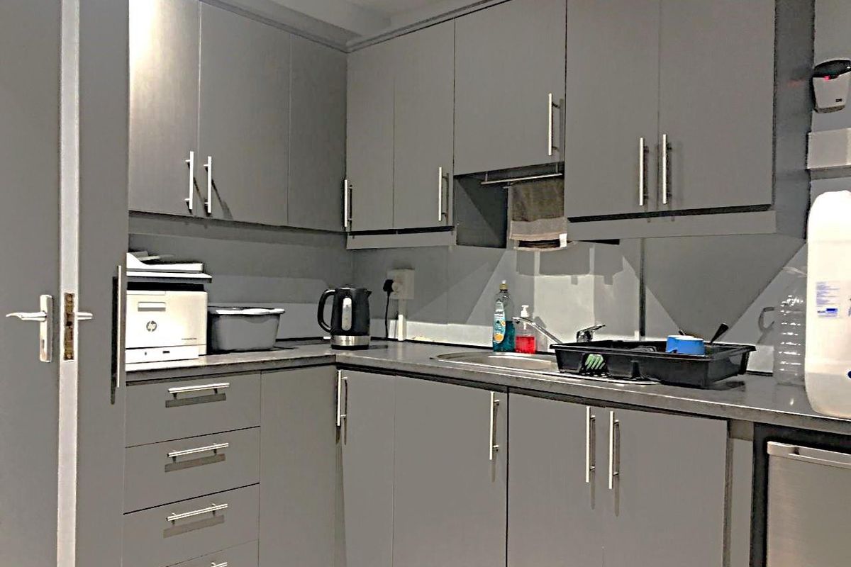 A compact commercial kitchenette featuring grey cabinetry, laminate countertops, and a stainless steel sink with a mixer tap.