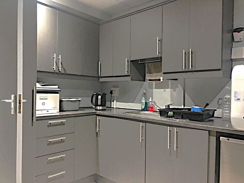 A compact commercial kitchenette featuring grey cabinetry, laminate countertops, and a stainless steel sink with a mixer tap.