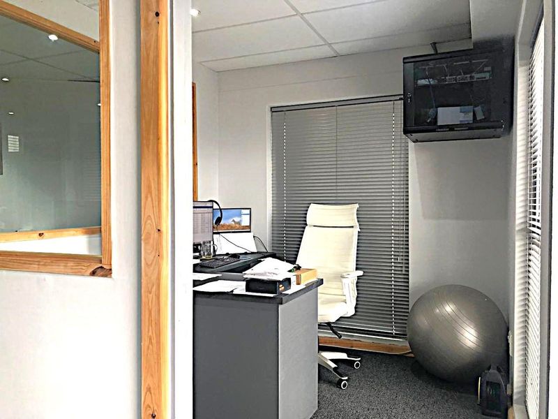 A functional commercial office space featuring a wall-mounted network server cabinet, venetian blinds, and recessed ceiling lighting.