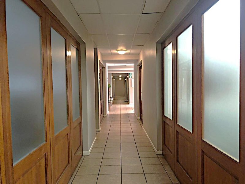 A commercial hallway featuring tiled flooring, suspended ceiling panels, and multiple wooden doors with frosted glass inserts.