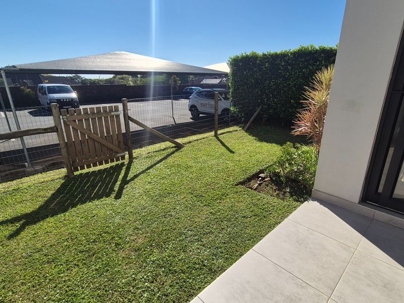 A private rear garden area featuring a tiled patio, a small lawn, and secure wire mesh fencing with a wooden gate.