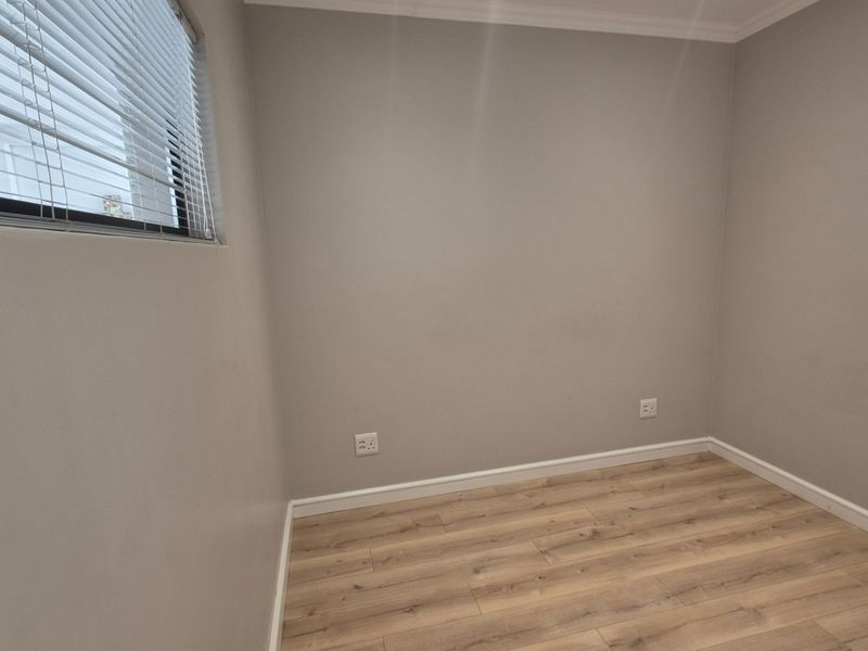A clean, empty bedroom featuring light-toned laminate flooring, neutral walls, and fitted venetian blinds, providing a versatile space ready for personalization.