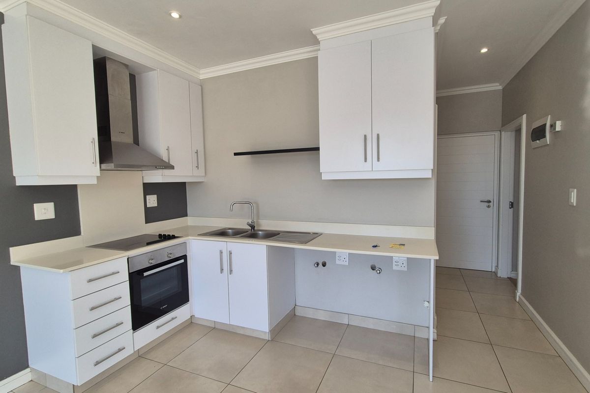 Modern kitchen featuring white cabinetry, stone countertops, integrated oven and hob, and tiled flooring in a clean, neutral space.