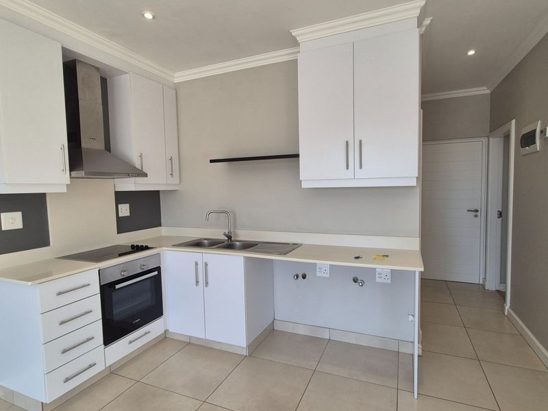 Modern kitchen featuring white cabinetry, stone countertops, integrated oven and hob, and tiled flooring in a clean, neutral space.