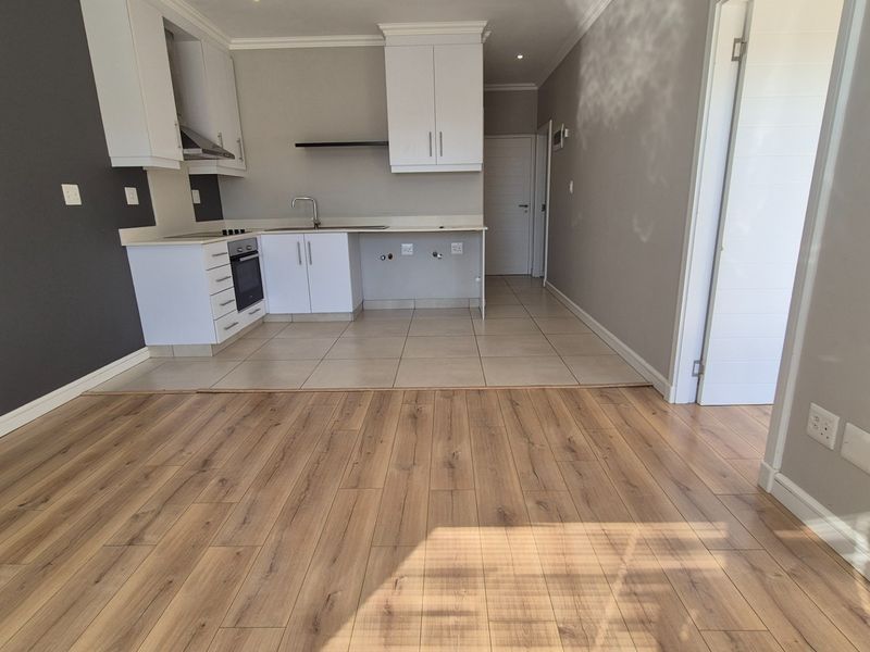 An open-plan living and kitchen area featuring modern white cabinetry, built-in oven, extractor fan, and a combination of laminate and tiled flooring.