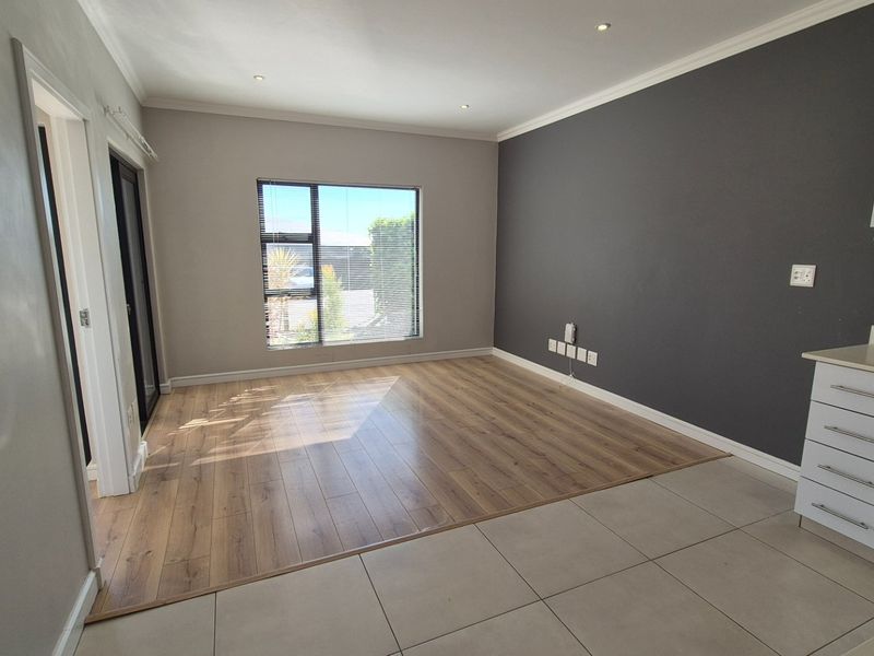 Bright open-plan living area featuring a combination of laminate and tiled flooring, modern kitchen cabinetry with built-in appliances, and large windows.