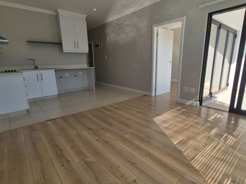 Modern open-plan living area featuring laminate flooring, a compact kitchen with built-in cabinetry, and large sliding doors leading to an outdoor space.