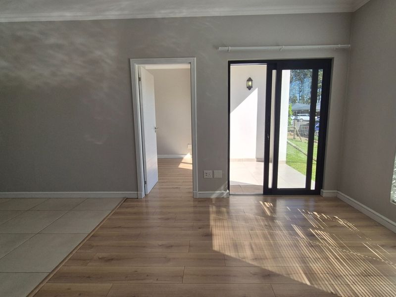 Bright and spacious living area featuring a mix of laminate and tiled flooring, with direct access to an outdoor patio through sliding glass doors.
