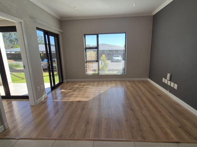A bright, empty living room featuring modern laminate flooring, an accent wall, and sliding glass doors providing access to the outdoor area.
