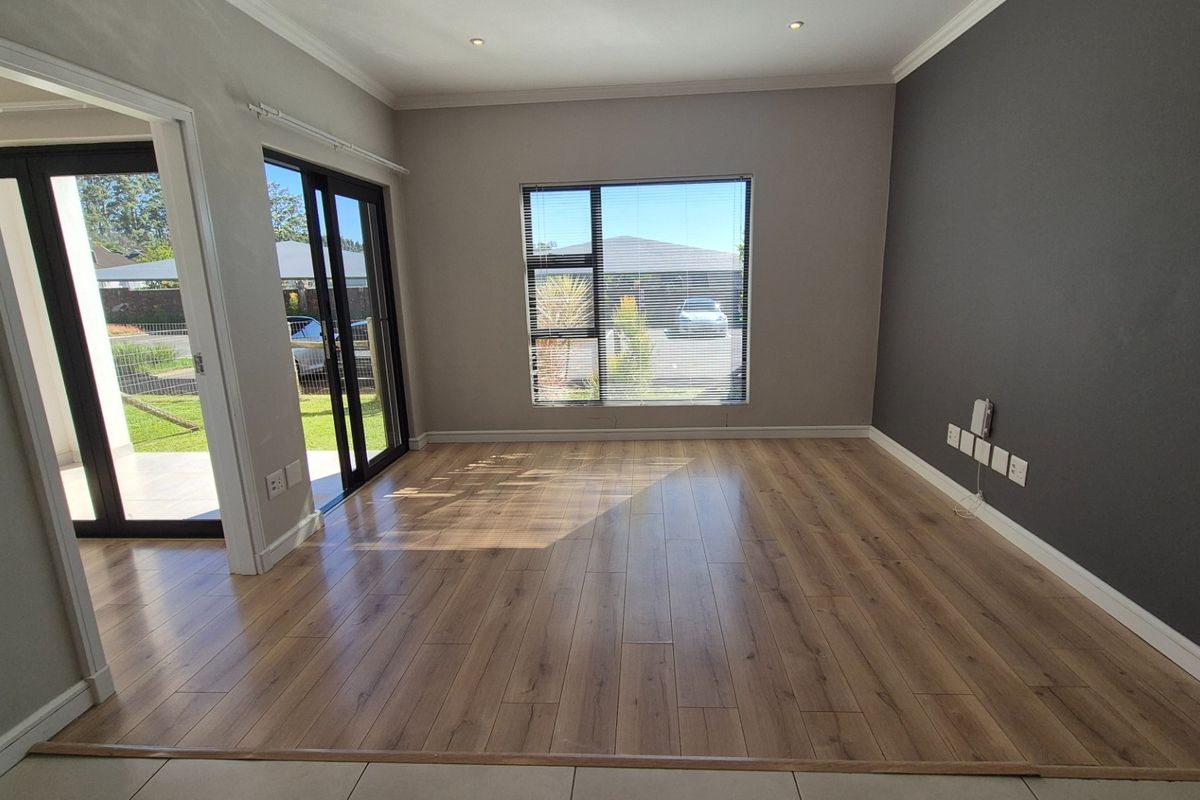 A bright, empty living room featuring modern laminate flooring, an accent wall, and sliding glass doors providing access to the outdoor area.