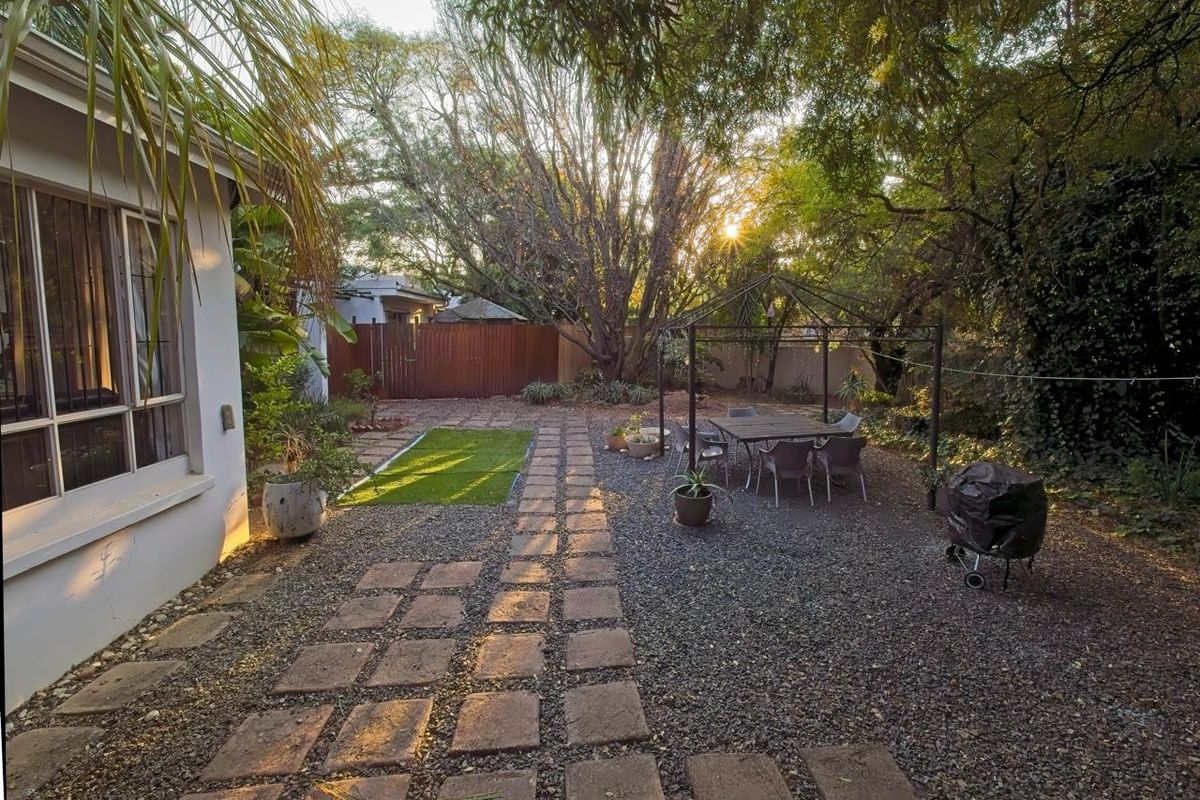 A private rear garden featuring a paved walkway, gravel landscaping, and mature trees, providing a tranquil outdoor space.