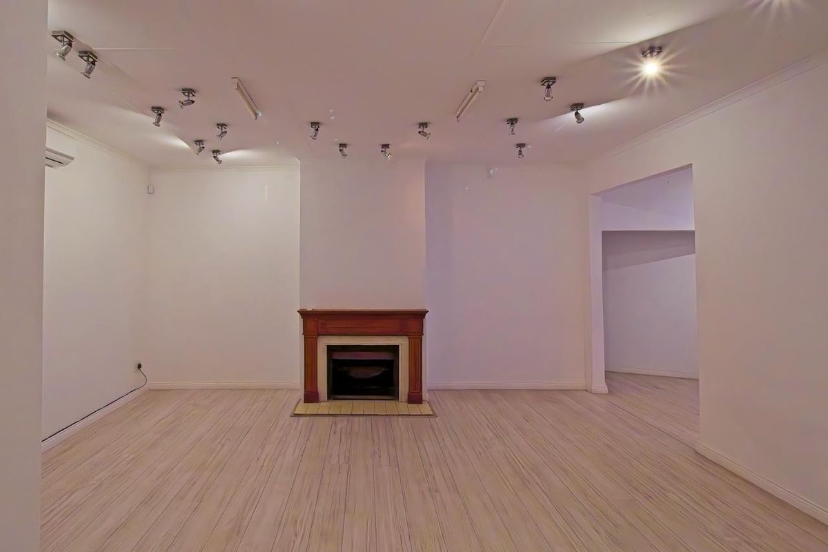 Spacious, empty living room featuring a central fireplace with a wooden mantelpiece, laminate flooring, and extensive ceiling-mounted spotlighting.