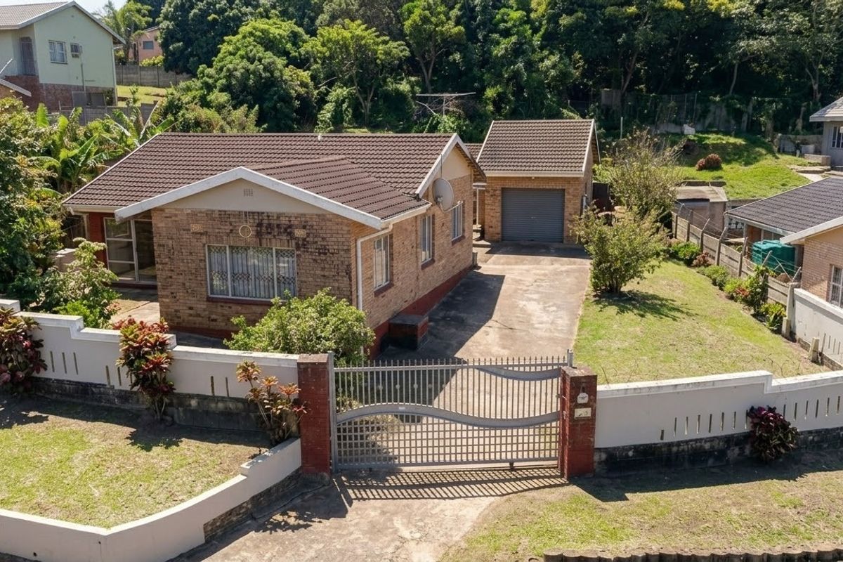 Aerial view of a detached brick house featuring a tiled roof, a separate garage, a concrete driveway, and a secure perimeter wall with a gate.