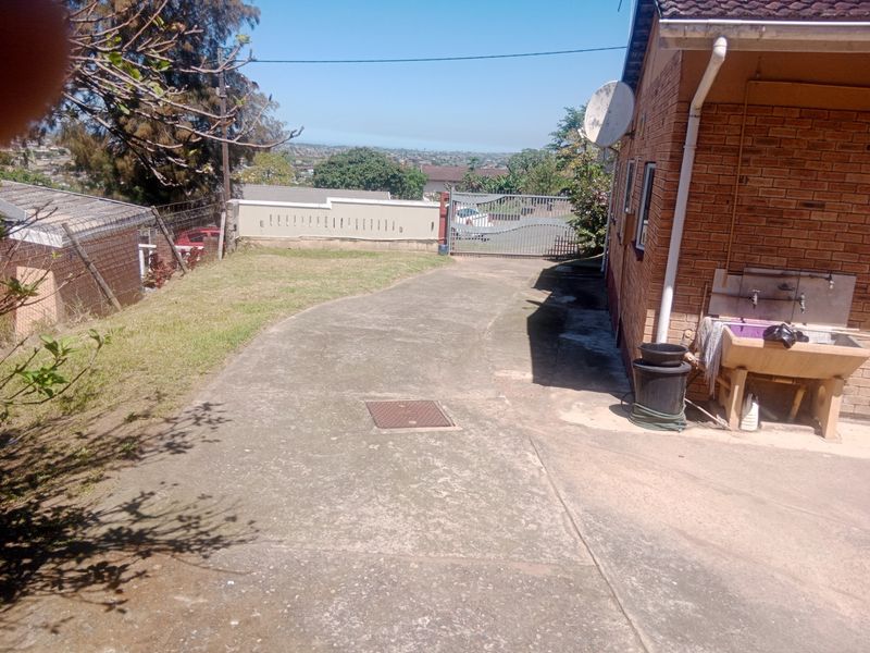 Rear exterior view featuring a concrete driveway, perimeter wall, metal gate, and an external utility sink attached to the brick house structure.