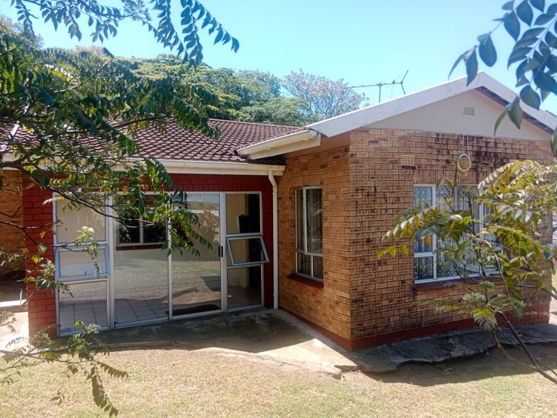 Rear view of a face brick house featuring aluminium sliding doors, security bars, and a concrete patio area set within a garden.