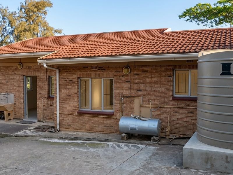 Rear exterior view of a face brick house featuring a tiled roof, external utility sink, water storage tank, and concrete paved area.