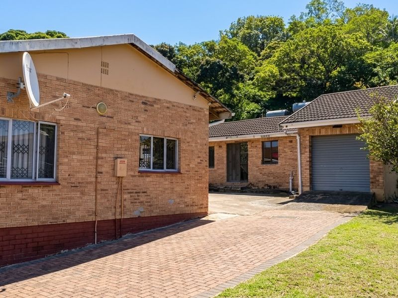 Rear view of the property featuring face brick construction, a paved driveway, and a single garage with a roller door.