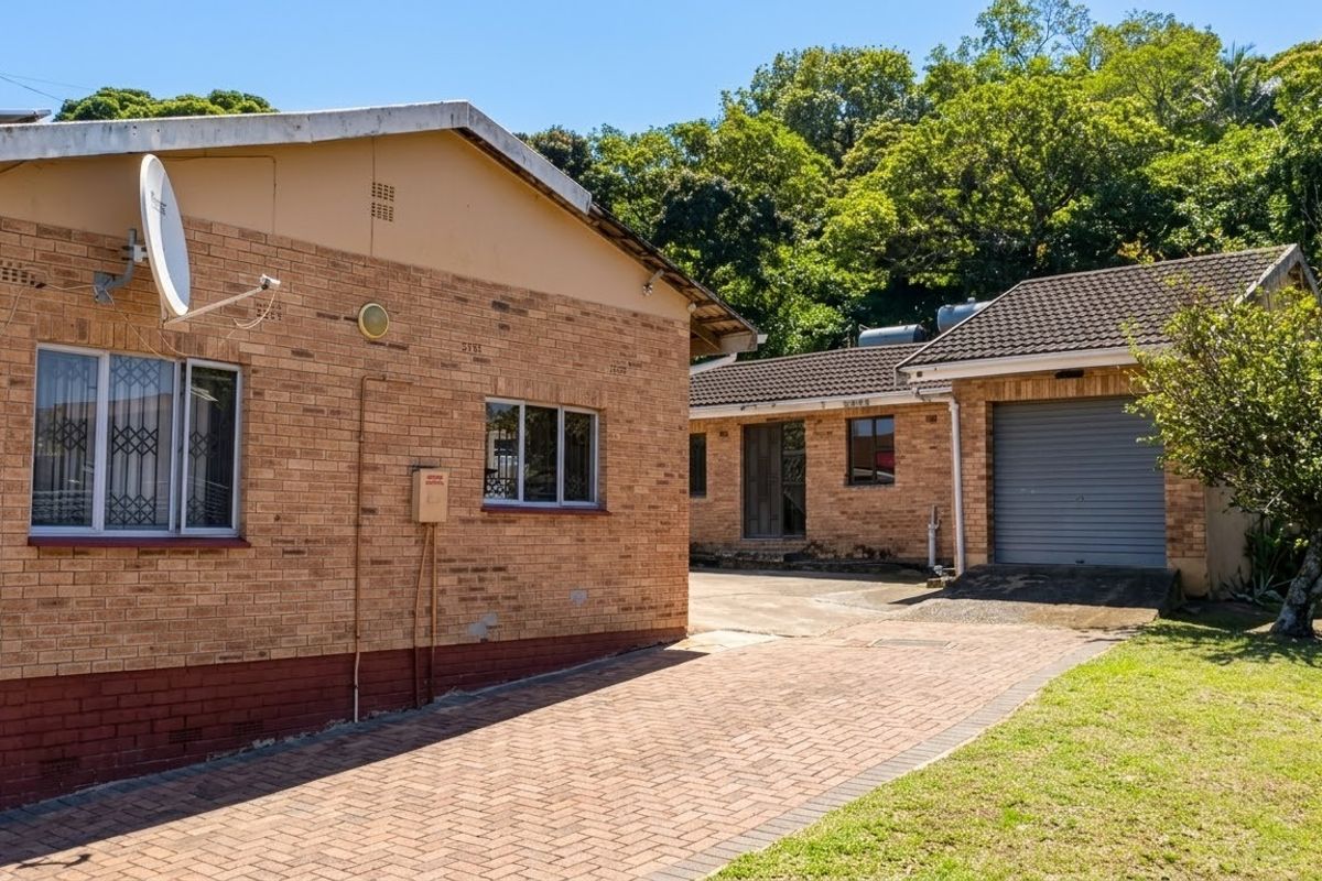 Rear view of the property featuring face brick construction, a paved driveway, and a single garage with a roller door.