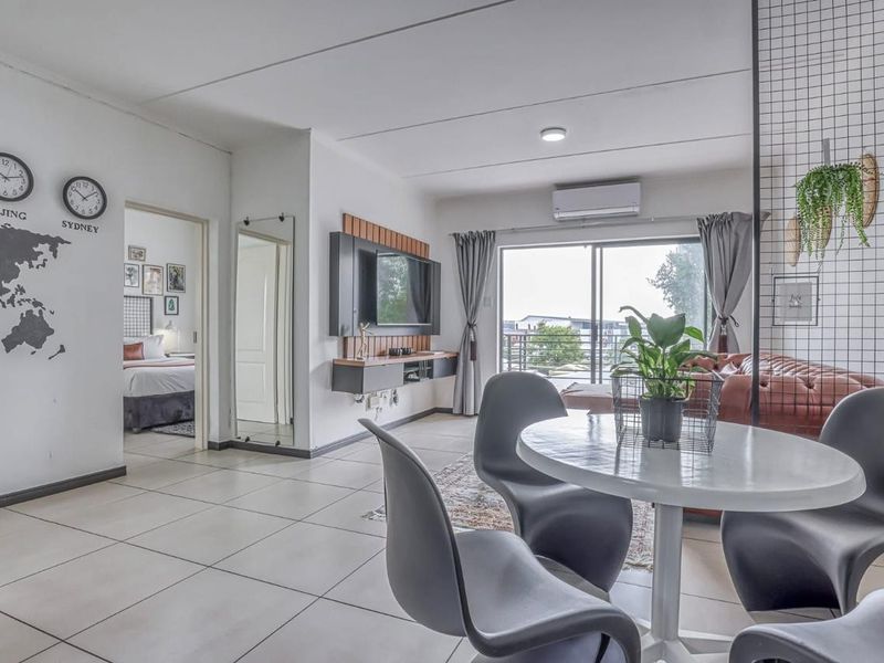 An open-plan living and dining area featuring tiled floors, a wall-mounted air conditioning unit, and a sliding glass door leading to a balcony.