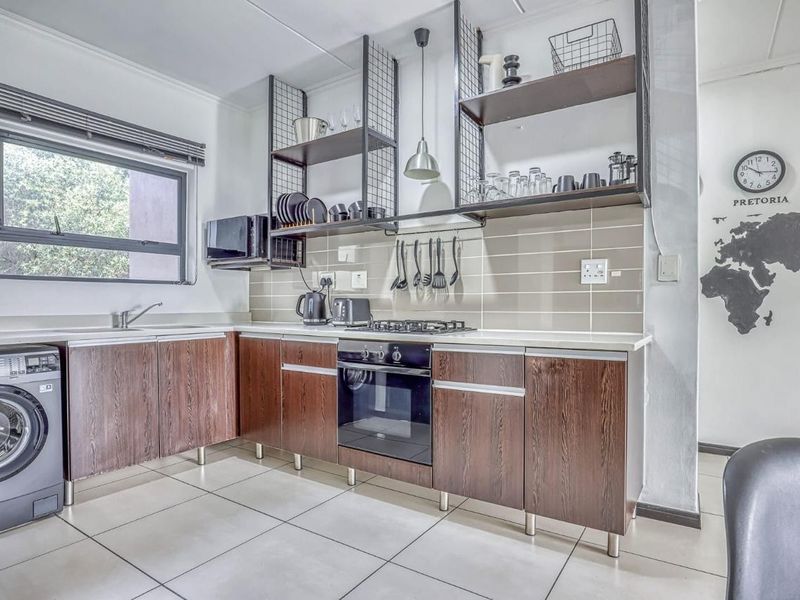Modern kitchen featuring dark wood-finish cabinetry, integrated appliances, gas hob, oven, and stylish open metal shelving with a neutral tiled backsplash.