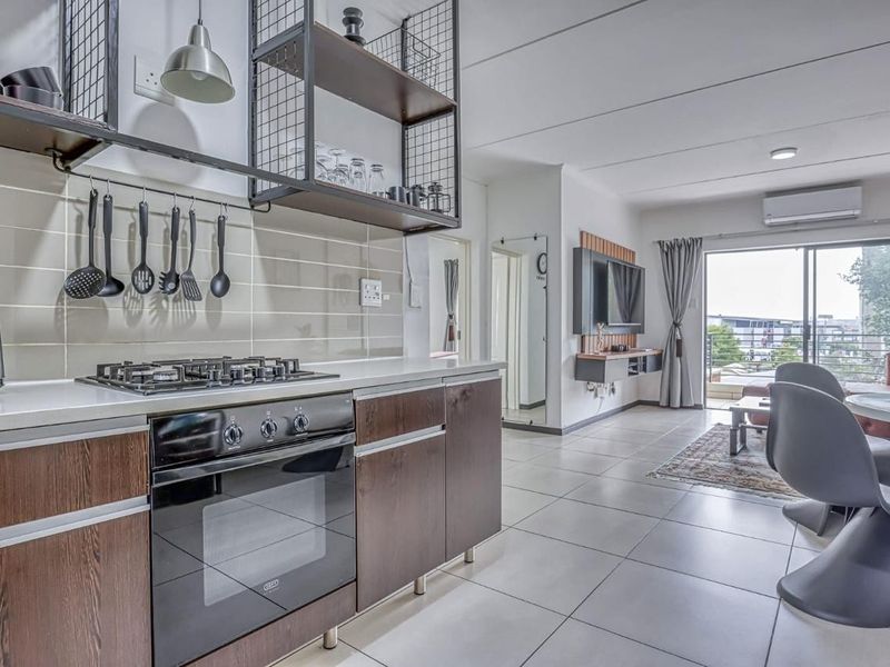 Modern open-plan apartment featuring a contemporary kitchen with gas hob, built-in oven, and tiled flooring, flowing seamlessly into a bright living area with balcony access.