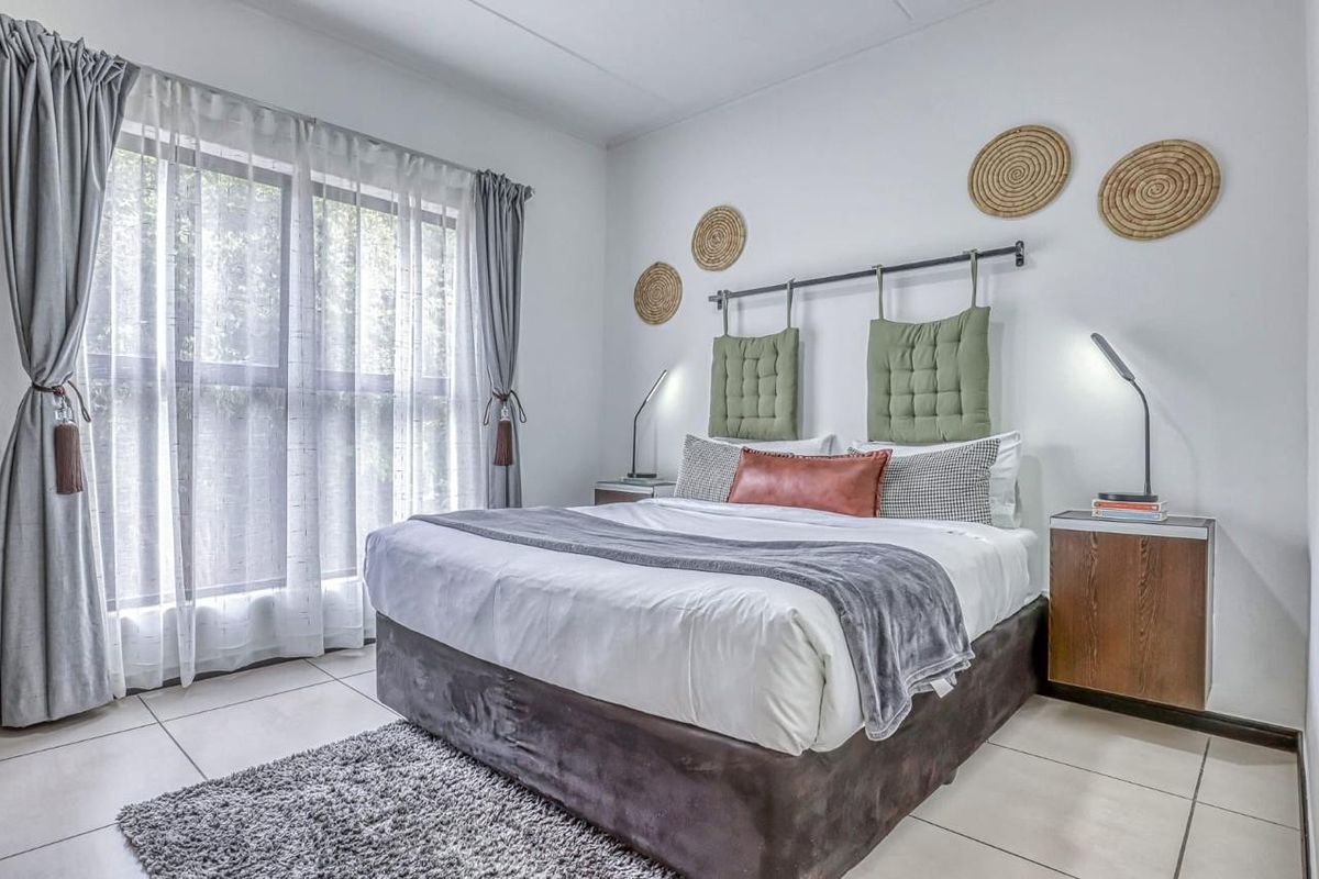 A bright and well-maintained bedroom featuring large windows with curtains and neutral tiled flooring.