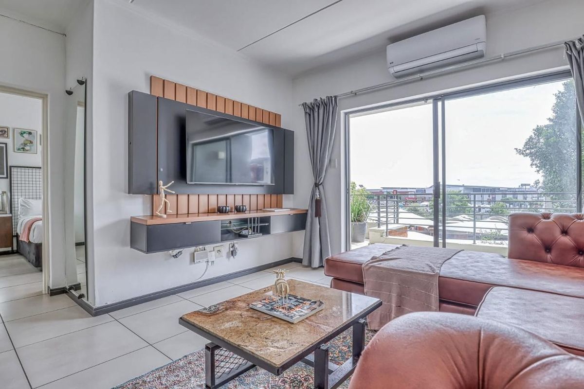 A well-lit living room featuring a modern wall-mounted media console, split-system air conditioning, and large sliding glass doors leading to a balcony.