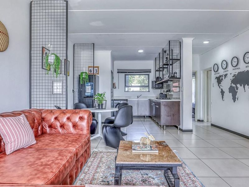 An open-plan living and kitchen area featuring tiled flooring, modern recessed lighting, and a functional kitchen layout with built-in cabinetry and sink.