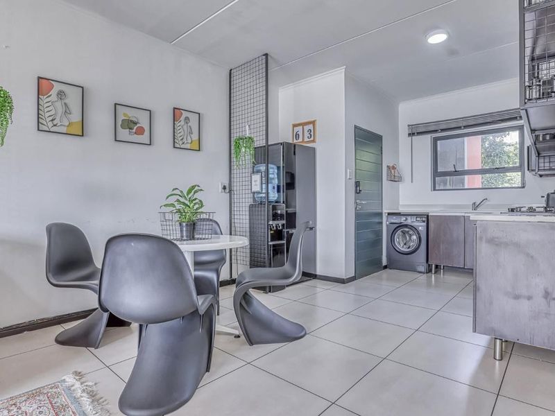 Modern open-plan living and kitchen area featuring tiled flooring, contemporary cabinetry, integrated laundry appliances, and a functional layout with a stylish metal room divider.