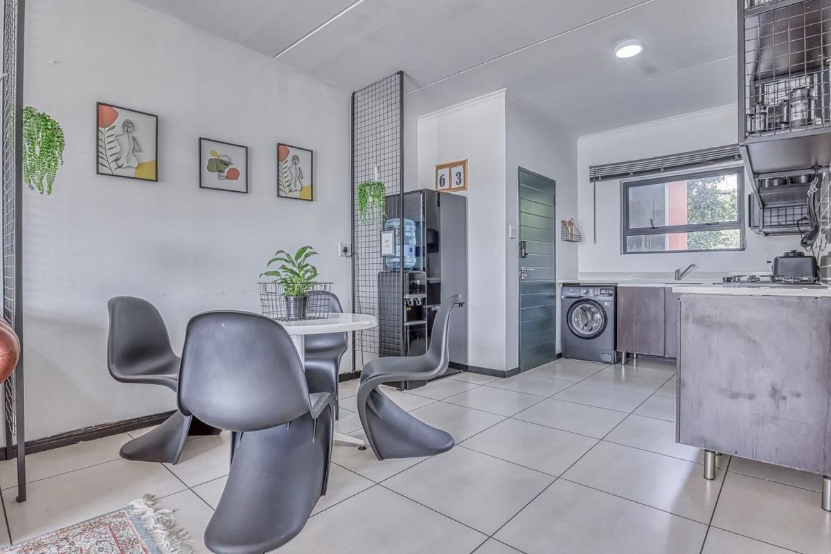 Modern open-plan living and kitchen area featuring tiled flooring, contemporary cabinetry, integrated laundry appliances, and a functional layout with a stylish metal room divider.