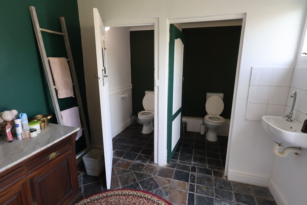 A functional bathroom featuring two separate toilet cubicles, a wall-mounted basin, and stone tile flooring with a vanity unit.