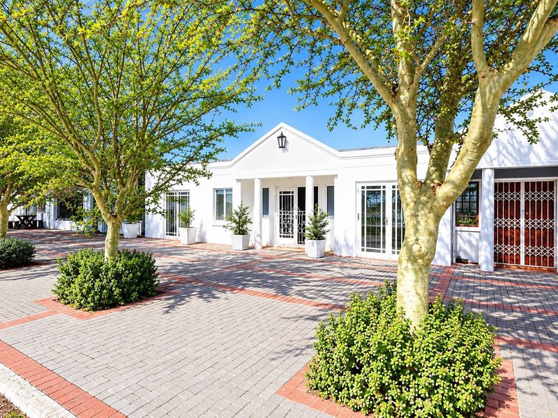 A well-maintained office building exterior featuring a paved entrance, mature trees, and secure access points with a clean, professional facade.