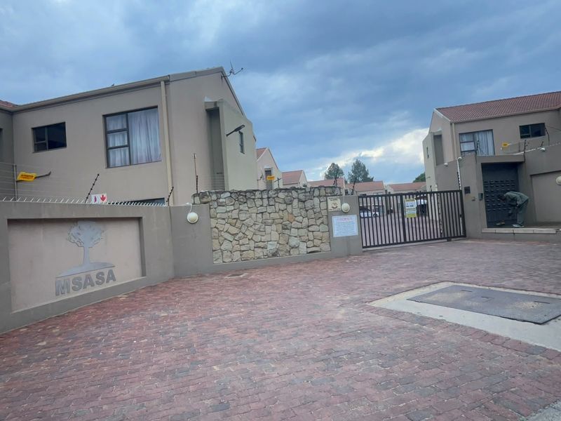 Front entrance view of the Msasa townhouse complex featuring a paved driveway, secure electric gate, and stone-clad boundary wall.