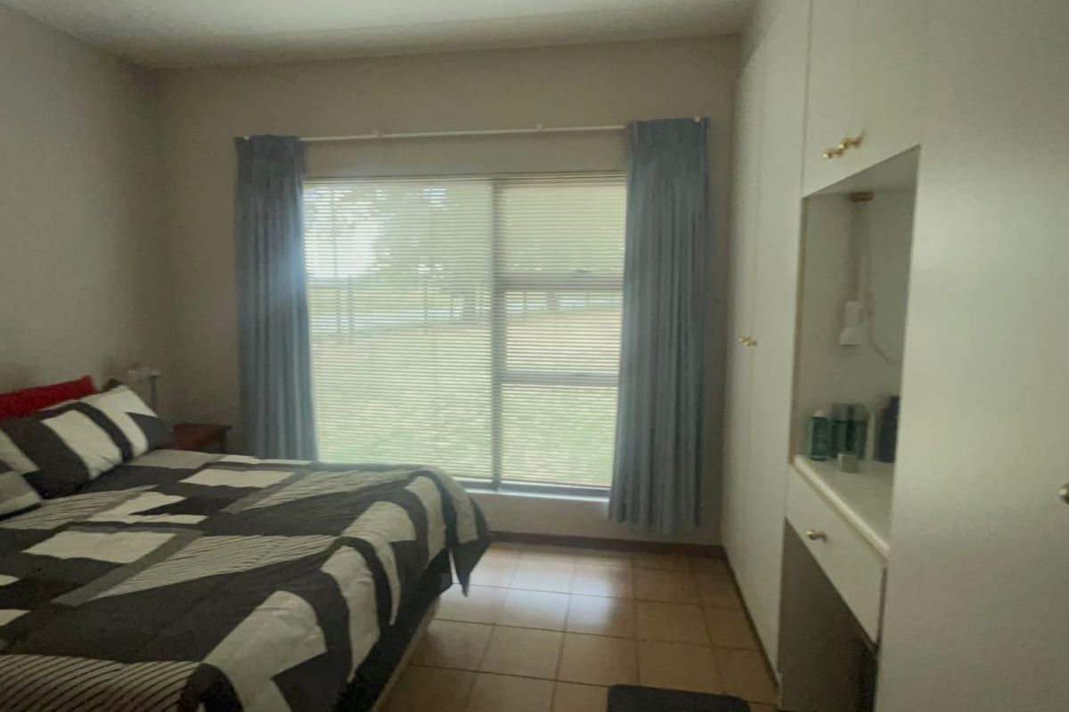 A bedroom featuring built-in cupboards with a vanity area, tiled flooring, and large windows with blinds.