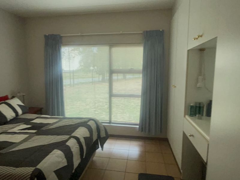 A bedroom featuring built-in cupboards with a vanity area, tiled flooring, and large windows with blinds.