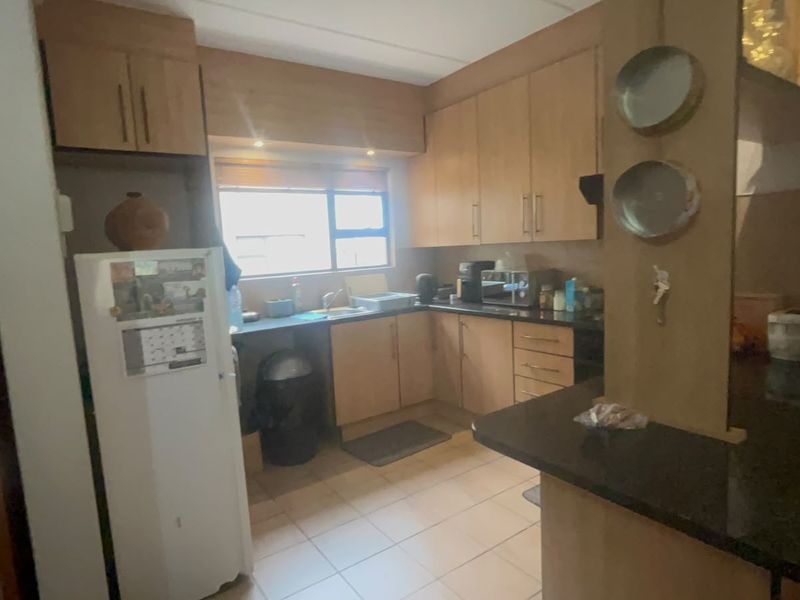 A functional kitchen featuring built-in wooden cabinetry, laminate countertops, a breakfast bar, and tiled flooring, offering a practical layout for daily use.