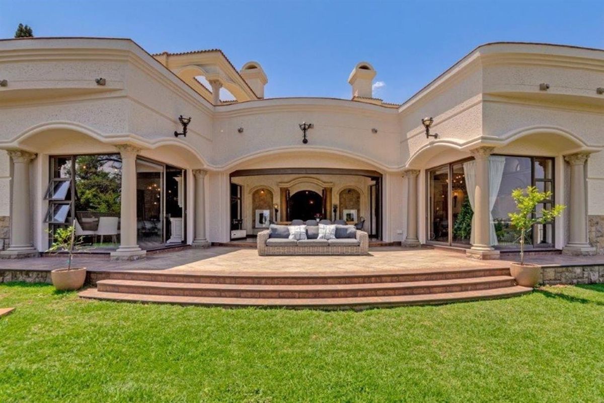 A spacious rear patio featuring stone tiling, decorative columns, and arched architectural elements, providing a seamless transition between the indoor living areas and the garden.