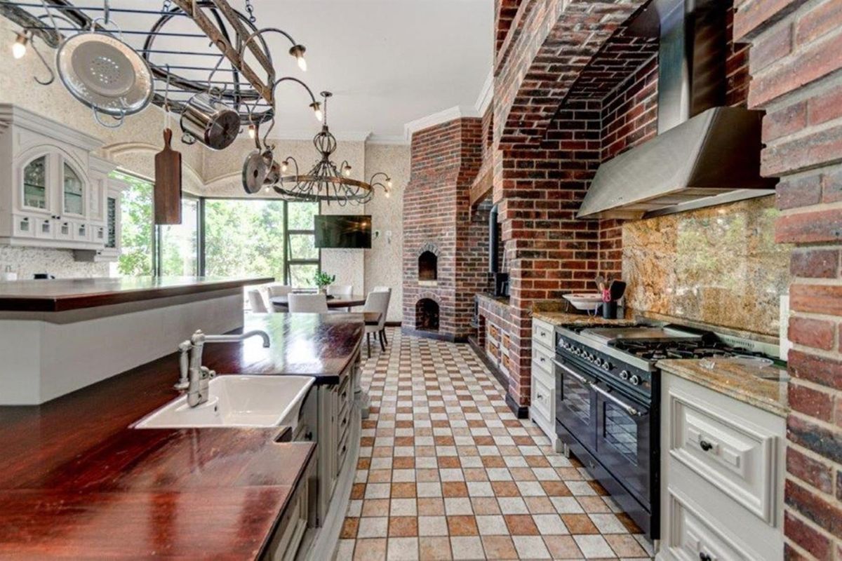 Spacious kitchen featuring a large brick fireplace, gas range with extractor, farmhouse sink, and a blend of granite and wooden countertops.